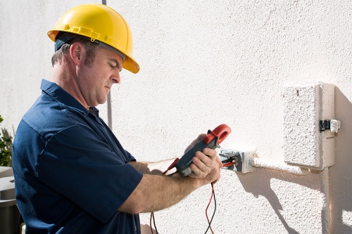 7 Tips for Year-Round Electrical Safety 1 Electrician in hard hat using a multimeter to check voltage on an electrical outlet, emphasizing electrical safety and maintenance.