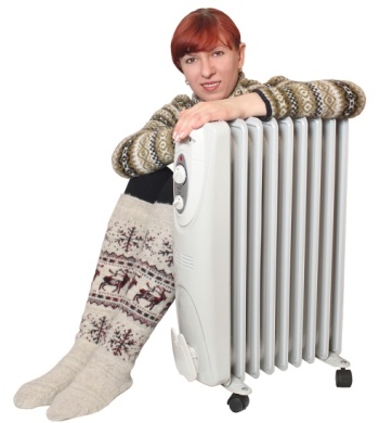 What are Baseboard Heaters? 5 Woman in cozy sweater and patterned socks sitting next to a baseboard heater, illustrating home heating comfort and supplemental warmth.