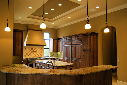 Choosing the Right Style of Recessed Lighting 3 Modern kitchen featuring recessed lighting and pendant fixtures, showcasing warm tones, wooden cabinetry, and a spacious layout, emphasizing stylish lighting solutions for residential design.