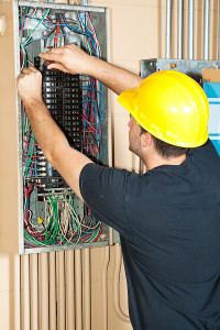Electrician working on a service panel installation, wearing a yellow hard hat and adjusting wiring in a residential electrical system, relevant to electrical services in Hockessin, DE.