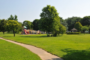 Hockessin park scene with playground equipment, walking path, and green trees, highlighting community space for families in Delaware.