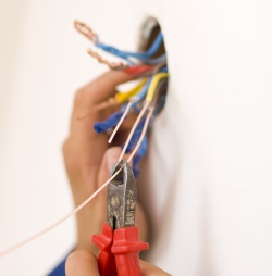 Electrician using wire cutters on copper and aluminum wiring during electrical service for home safety.